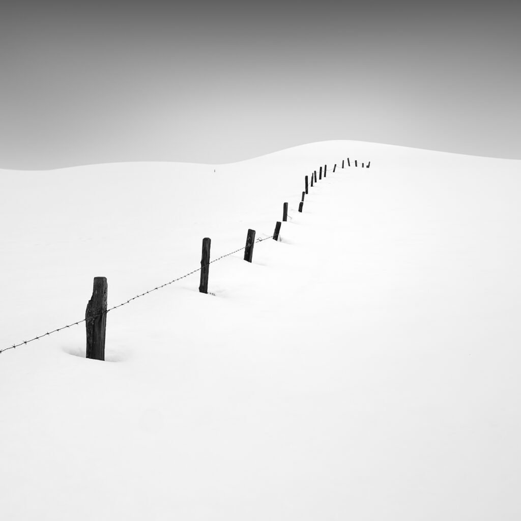 A row of poles in the snow on a hill with barb wire in between
